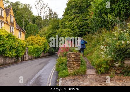 Wanderer gehen auf einem Waldweg entlang der Hauptstraße in `Castle Combe, in Cotswold, Großbritannien Stockfoto